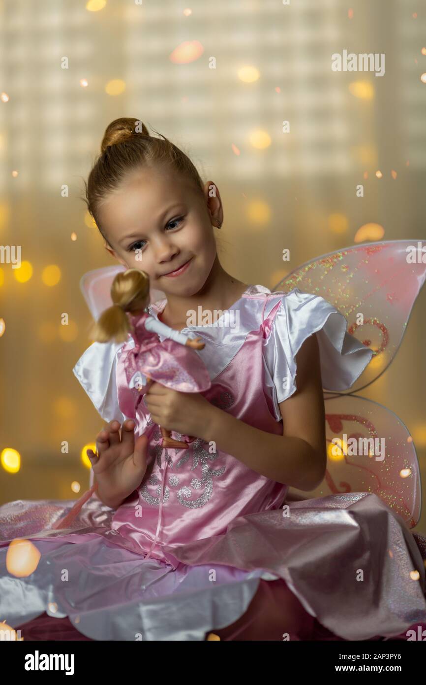 Poco fairy en un vestido rosado jugando con una muñeca Foto de stock