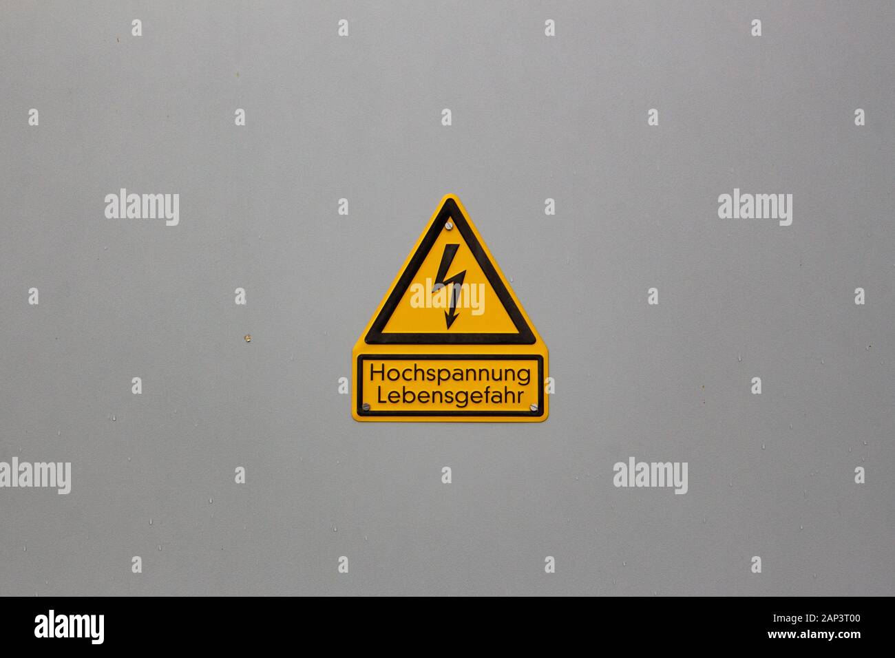 Alemán la señal de advertencia "Peligro de alta tensión a la vida", en alemán "Hochspannung, Lebensgefahr' en el centro de una planicie pared con copyspace alrededor Foto de stock