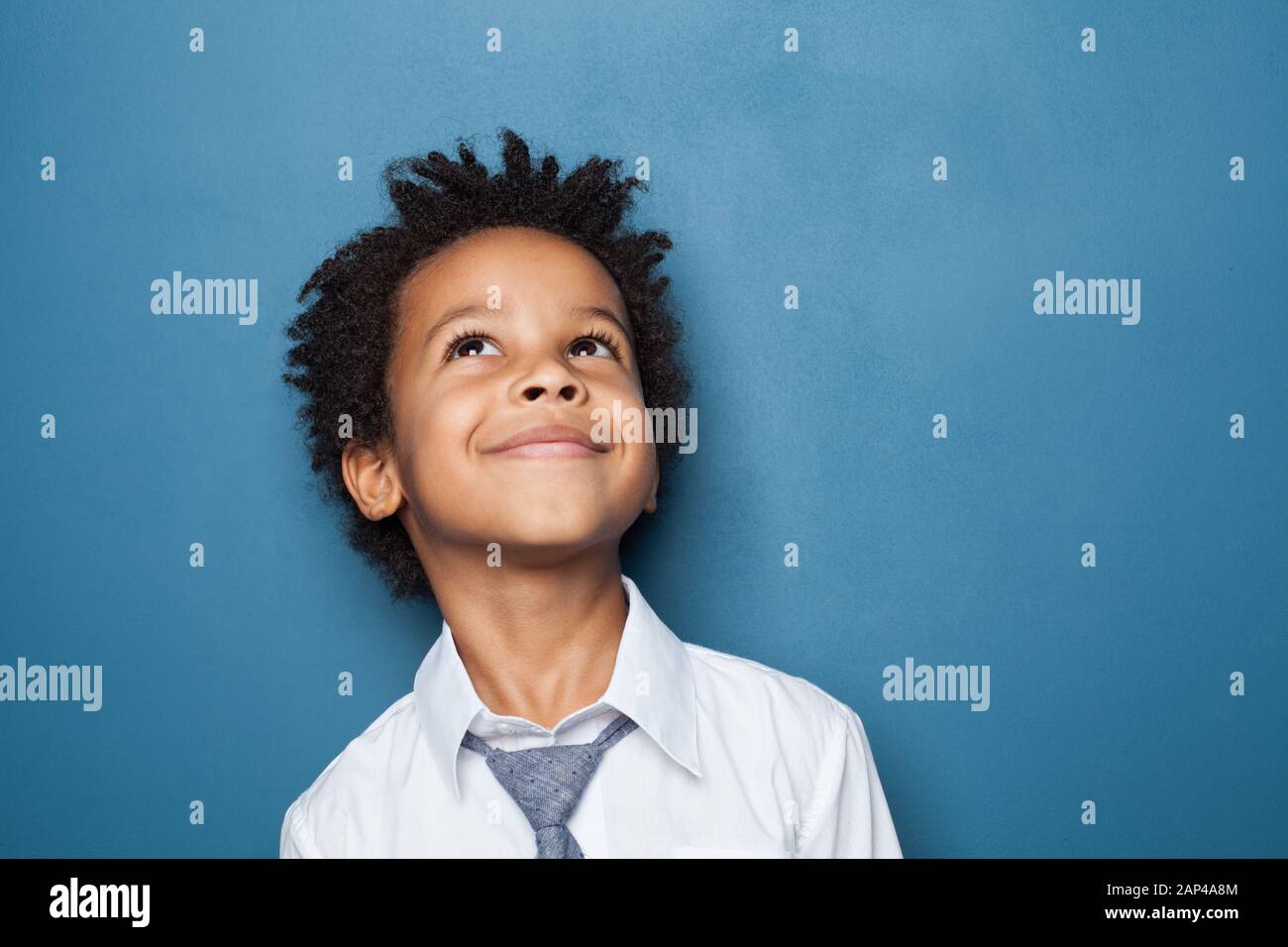 Feliz niño escuela niño retrato. Niño pequeño mirando hacia arriba sobre fondo azul Foto de stock
