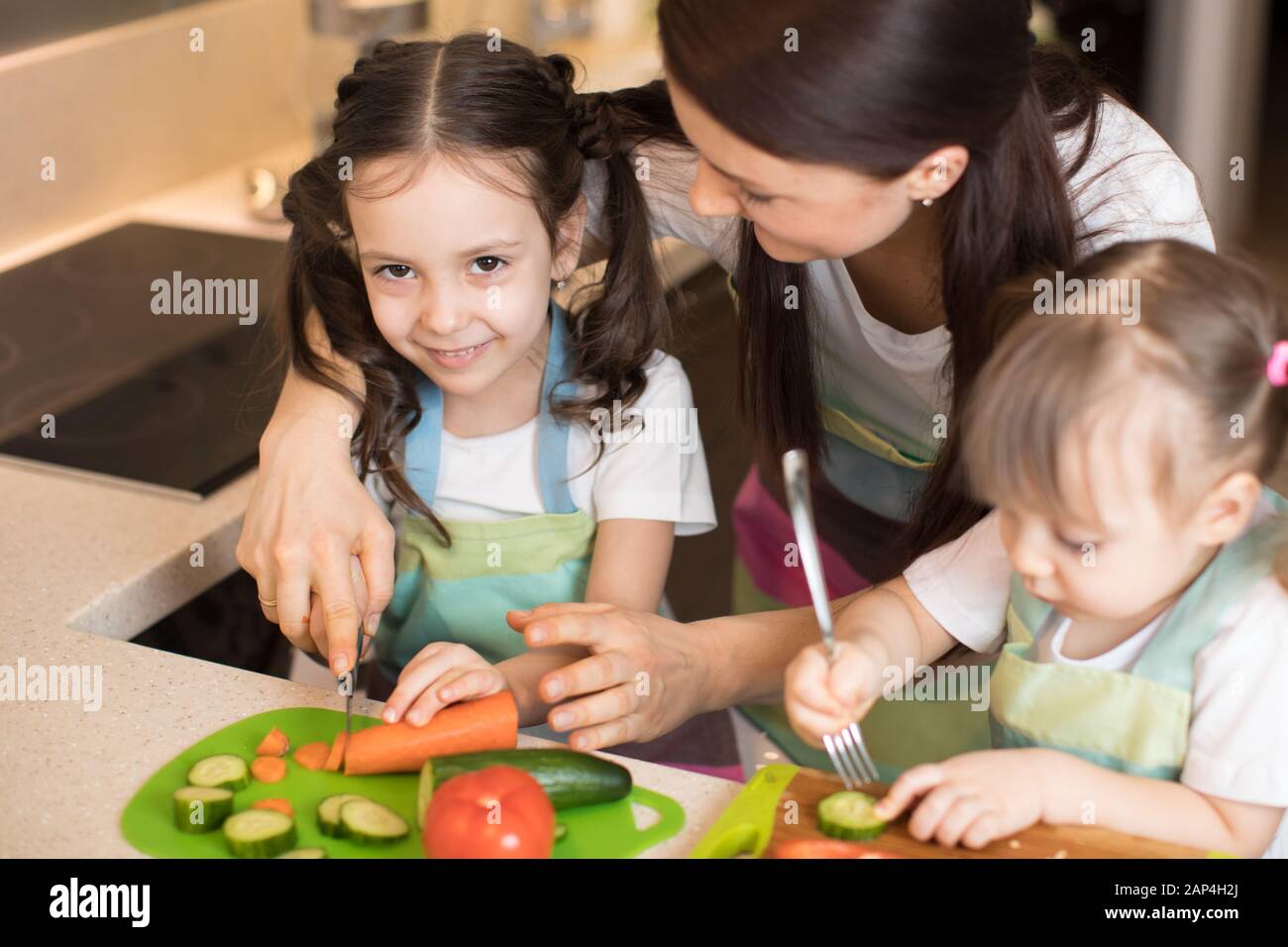 Mamá picando verduras con sus hijas en una cocina familiar. Foto de stock