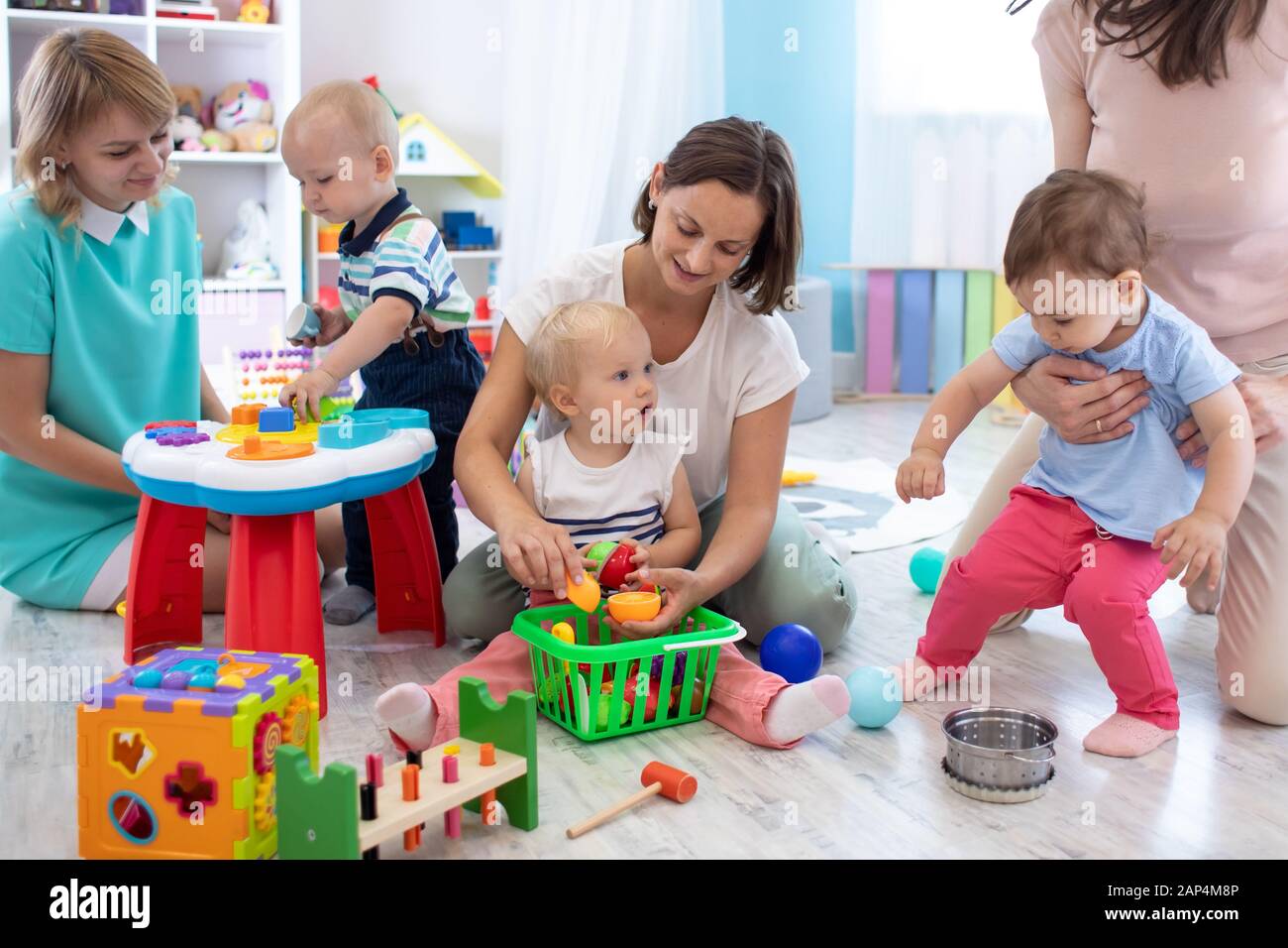 Un grupo de madres tienen un pasatiempo divertido con sus bebés niños pequeños en el cuarto de juegos en el cuidado de los niños Foto de stock