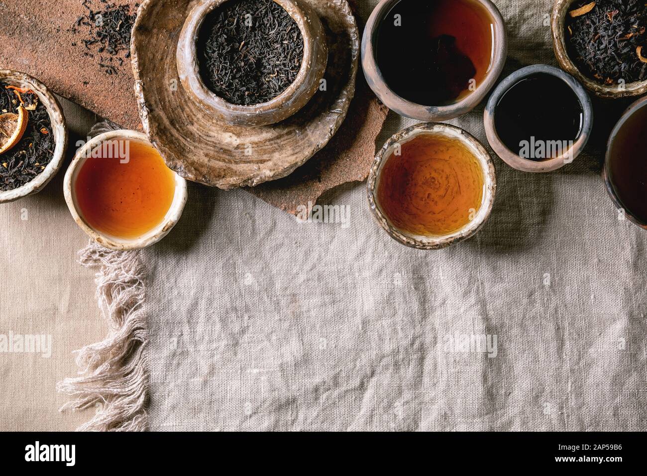 Variedad de té caliente y seco en verde y negro, en estilo tradicional y wabi sabi refractario artesanía cerámica vasos y copas, servidas en tela de lino como backgrou Foto de stock