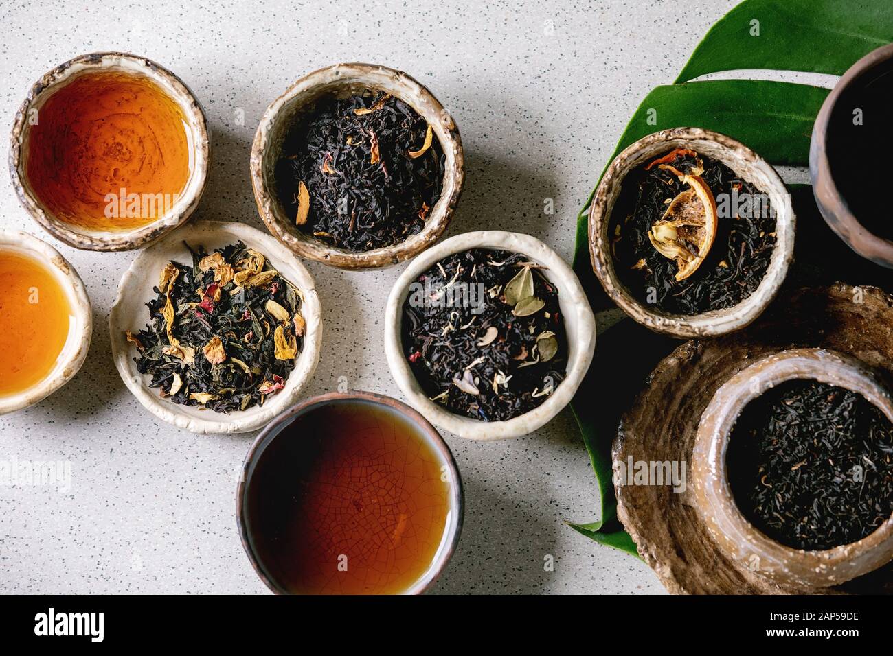 Variedad de té caliente y seco en verde y negro, en estilo tradicional y wabi sabi refractario artesanía cerámica vasos y copas, en hoja monstera exóticos más gris Foto de stock