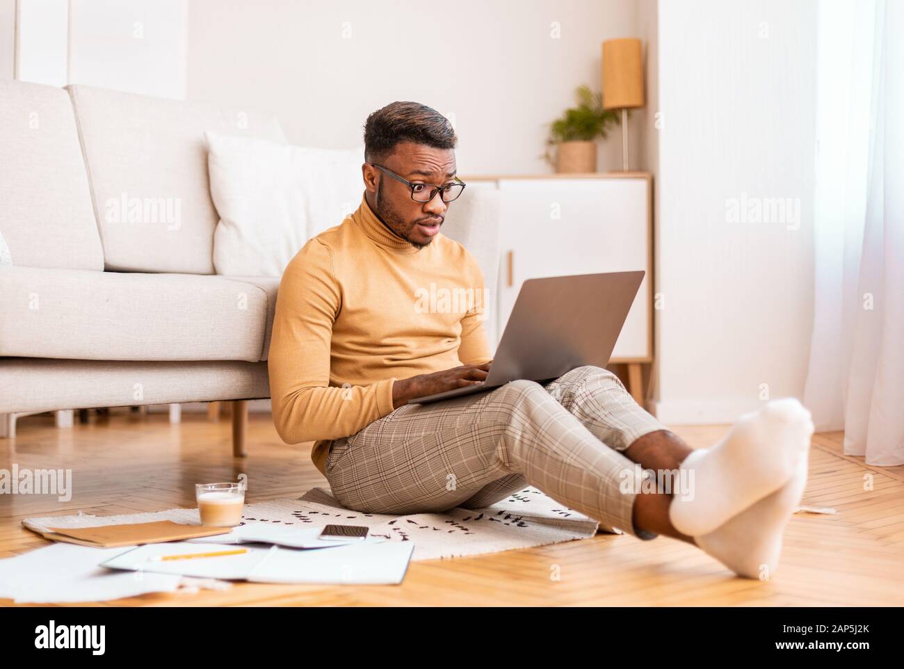 El hombre conmocionado leyendo noticias en el portátil sentado en el piso interior Foto de stock