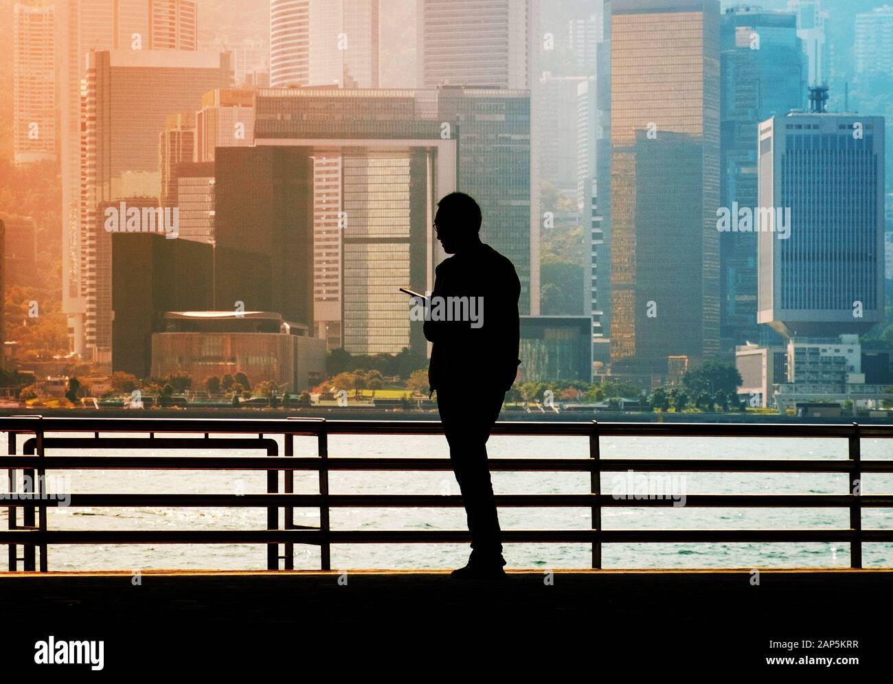 Silueta de un hombre que busca en el teléfono móvil con la Isla de Hong Kong de fondo del horizonte de la ciudad Foto de stock