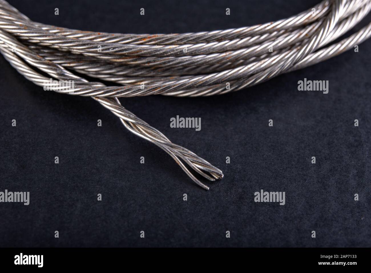 Cuerda de acero enrollada en un lazo. Accesorios en un taller doméstico. Fondo oscuro Foto de stock