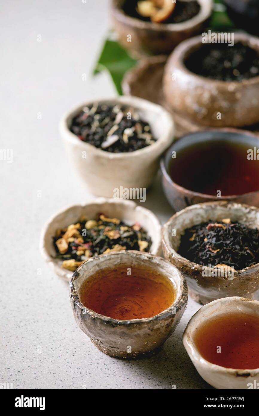 Variedad de té caliente y seco en verde y negro, en estilo tradicional y wabi sabi refractario artesanía cerámica vasos y copas más gris de fondo moteado. Clos Foto de stock