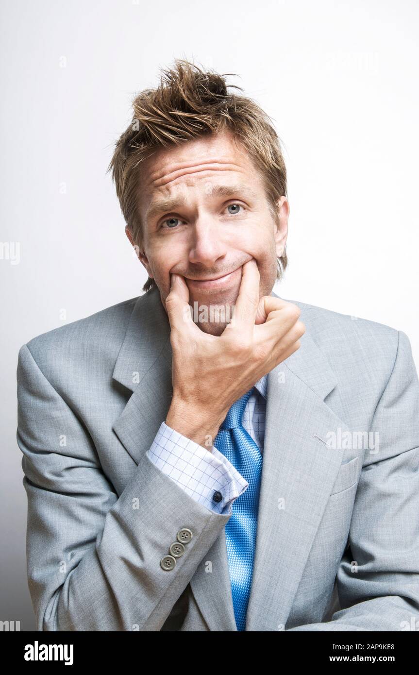 Cansado del empresario forzando una sonrisa sujetando las esquinas de su boca con sus dedos Foto de stock