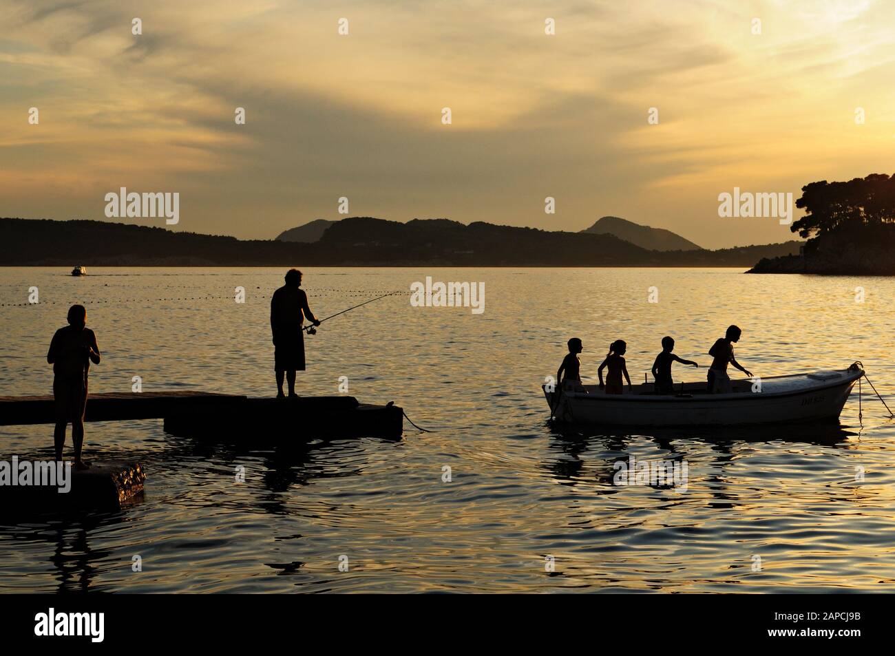 Siluetas de niños en un barco y pescador al atardecer en Dubrovnik (península de Lapad), Croacia Foto de stock
