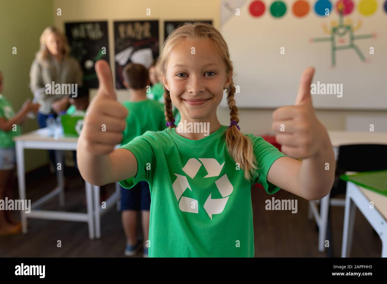 Colegiala con una camiseta verde con un logotipo de reciclaje blanco con sus pulgares hacia arriba Foto de stock