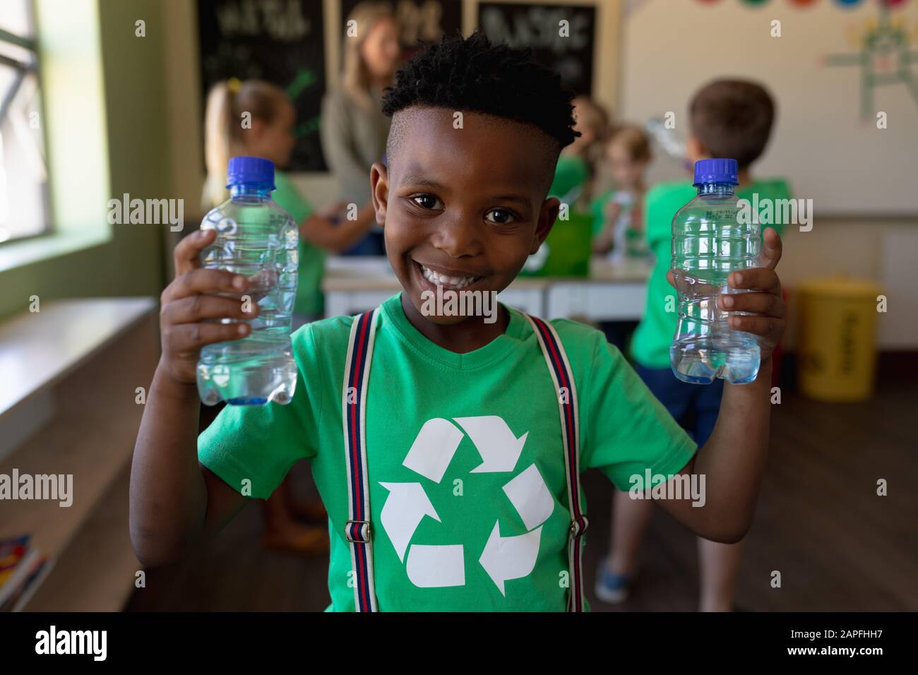Niño escolar que lleva una camiseta verde con un logotipo de reciclaje blanco en ella y que sostiene dos aguas de plástico bo Foto de stock