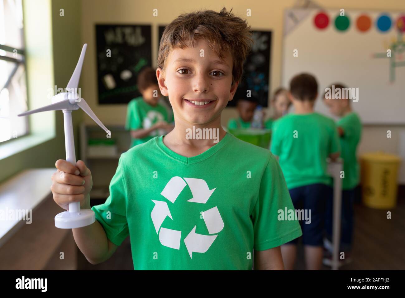 Niño escolar que lleva una camiseta verde con un logotipo de reciclaje blanco en ella y que sostiene turbi viento en miniatura Foto de stock