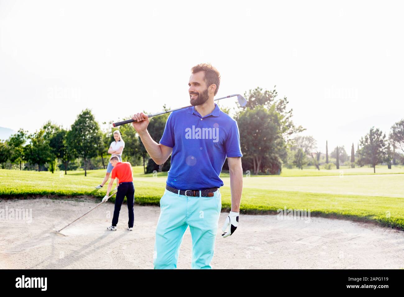 Hombre llevando club de golf en el campo de golf, amigos jugando al golf en el fondo Foto de stock