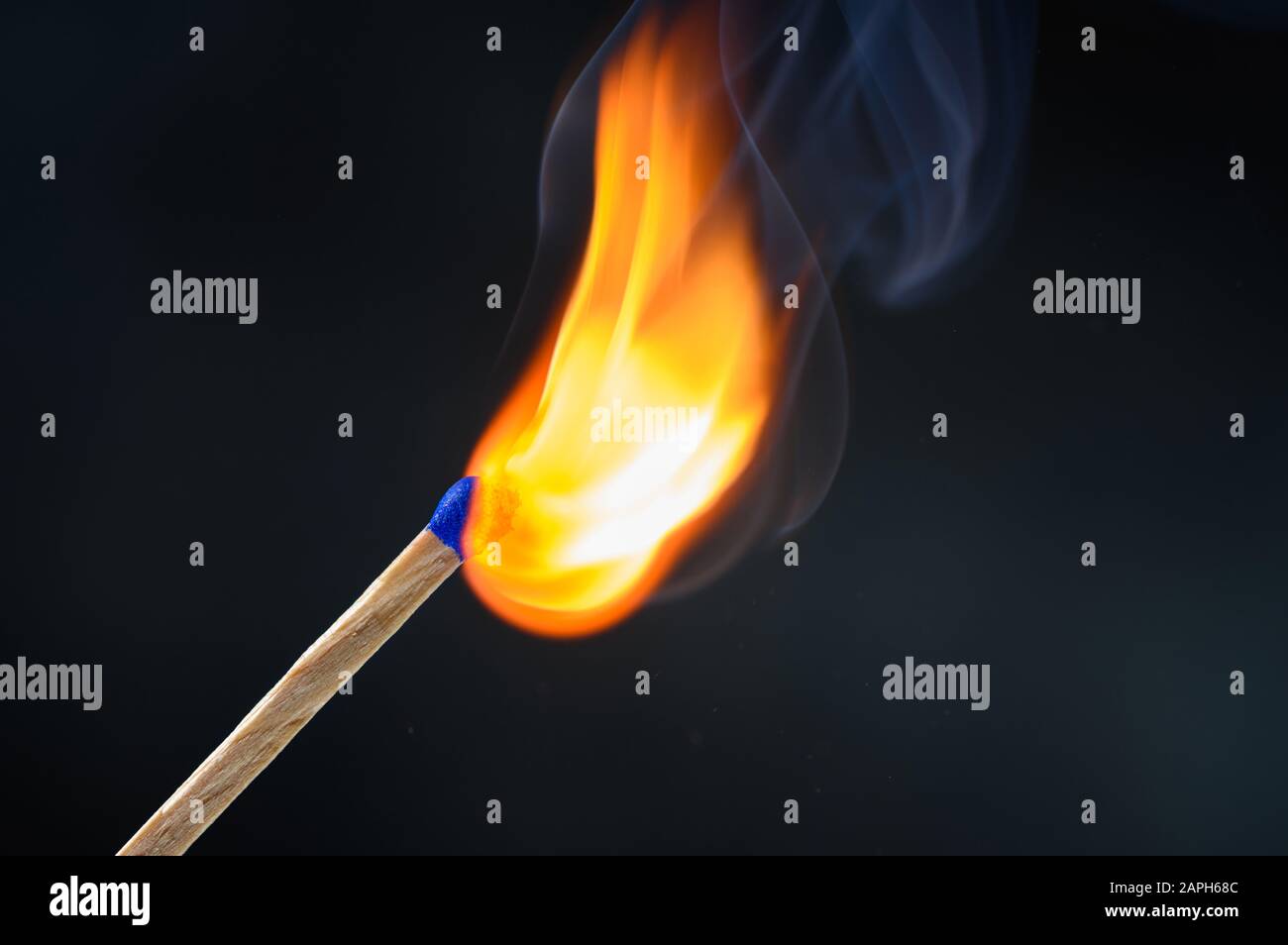 Palo de madera a juego con la cabeza azul encendido y quema fuego grande brillante sobre fondo negro. Foto de stock