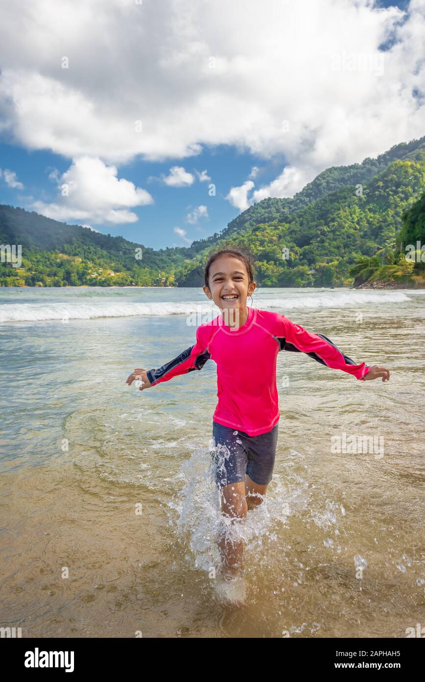 Niña jugando en Maracas Bay Beach Trinidad y Tobago divirtiéndose chapoteando en las olas Foto de stock