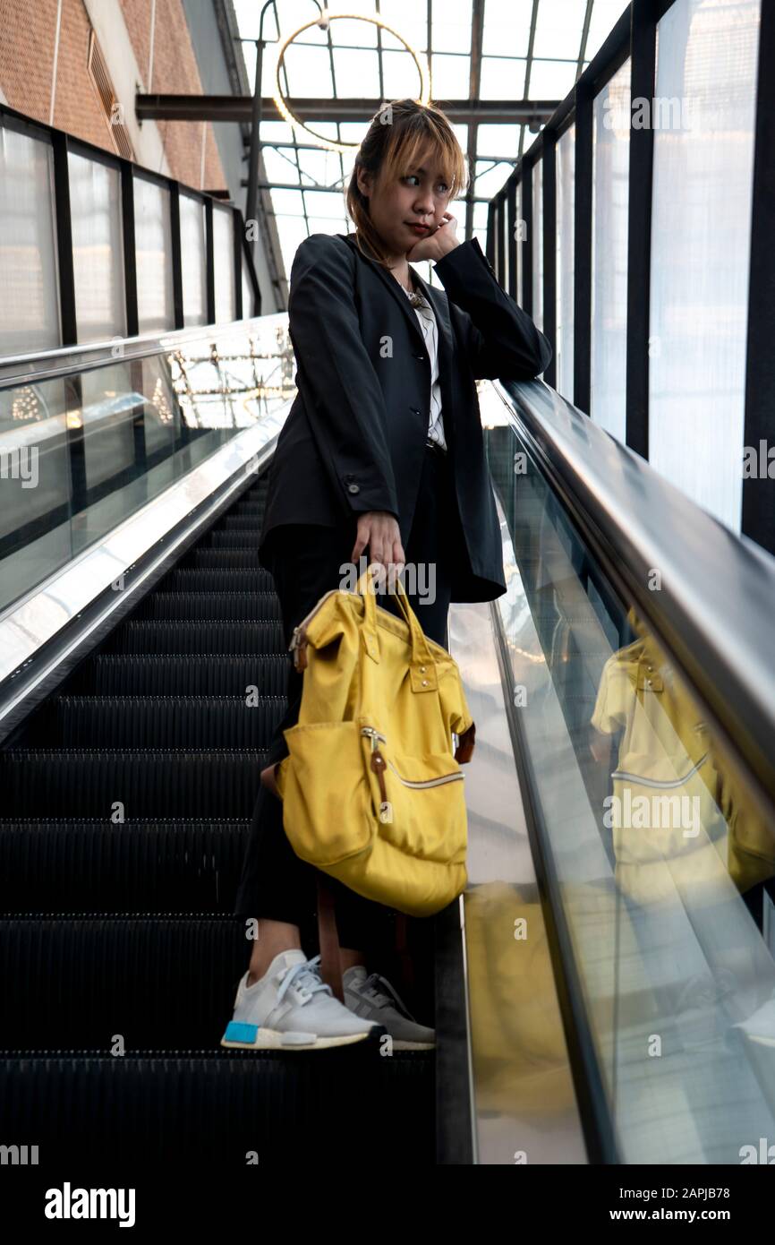 Mujer rubia confundida en ropa semi-formal de pie en la escalera mecánica  sosteniendo mochila amarilla, ella frunció el ceño esperando a su amigo  Fotografía de stock - Alamy