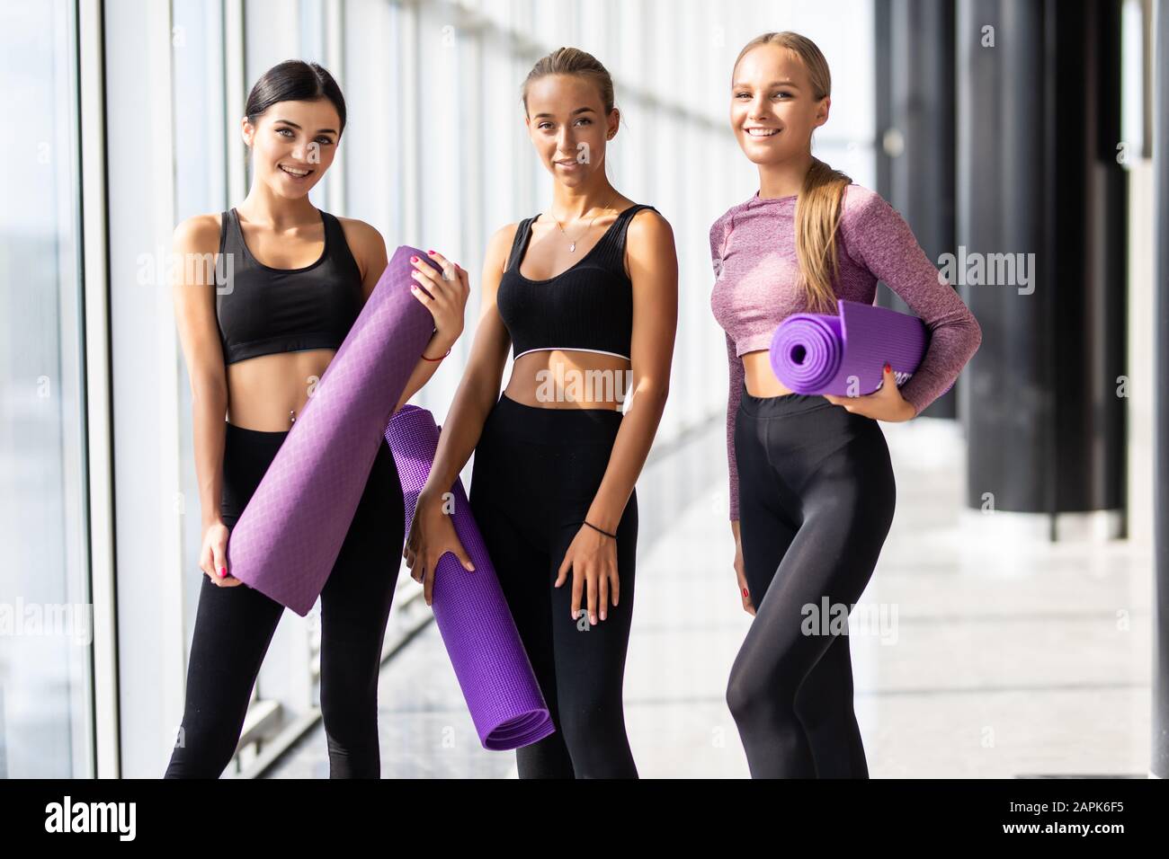 Tres de fitness en ropa deportiva de pie contra la pared en gimnasio Fotografía de stock - Alamy