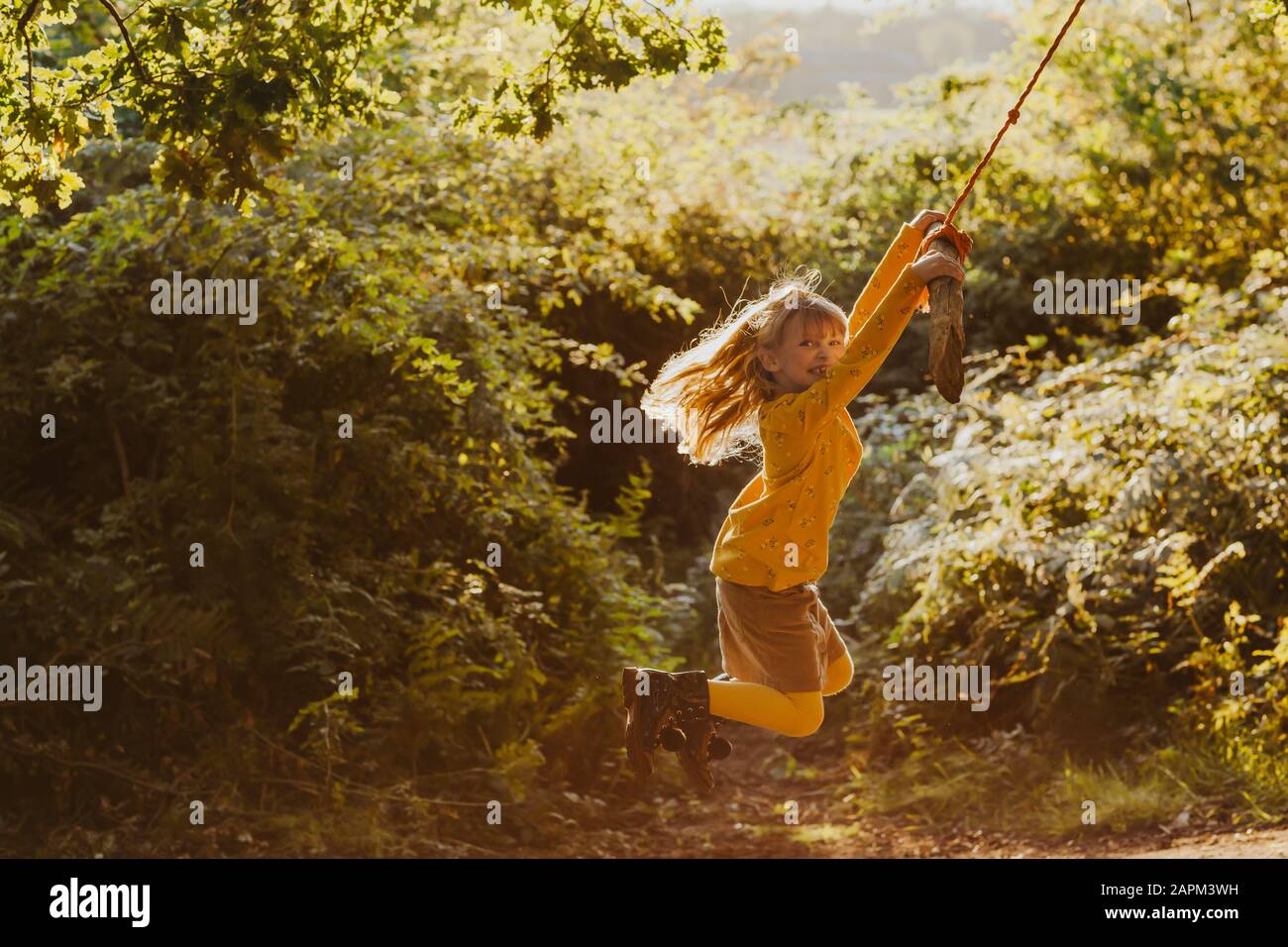 Feliz niña balanceándose en un columpio de cuerda en la naturaleza Foto de stock