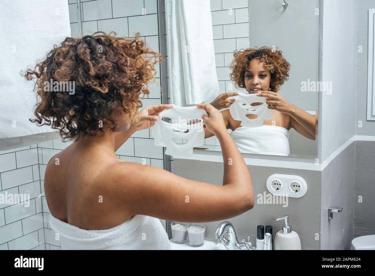 Mujer joven en el baño aplicando máscara facial Foto de stock