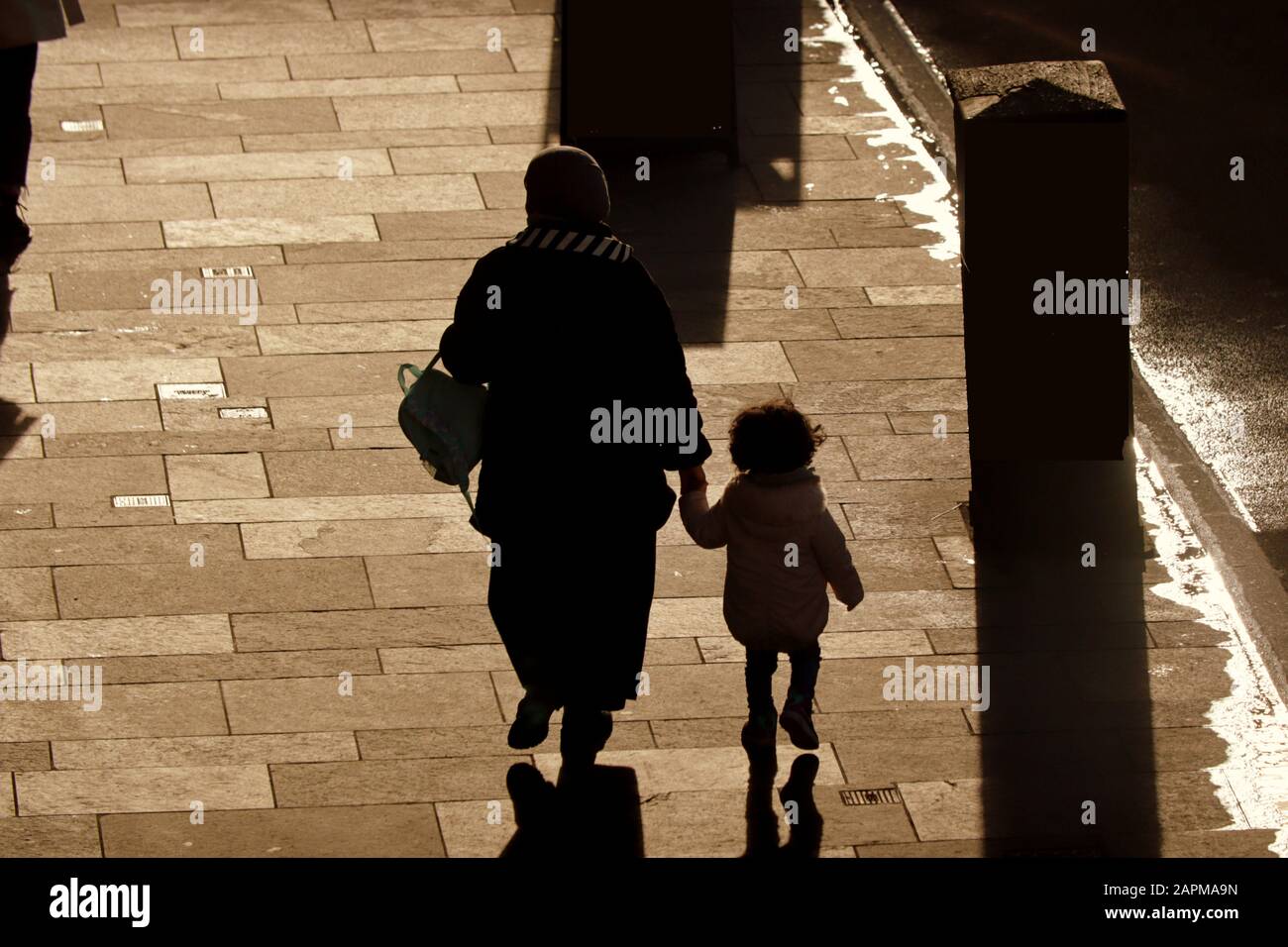 Extranjeros, inmigrantes o solicitantes de asilo en las calles del Reino Unido. Madre de familia con niño caminando en silueta Foto de stock