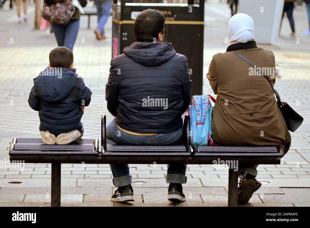 Extranjeros, inmigrantes o solicitantes de asilo en las calles del Reino Unido. Familia con niño sentado en el banco Foto de stock