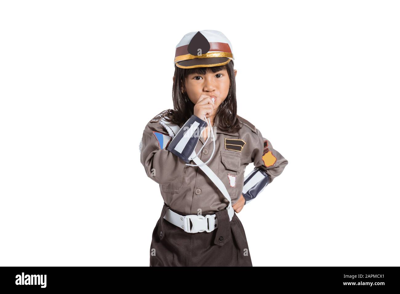 Niña asiática que lleva un uniforme de policía con un silbato que sopla sobre un fondo aislado Foto de stock