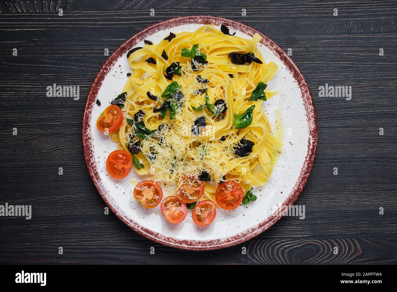 Vista superior de tagliatelle con tomate, parmesano, aceitunas picadas y albahaca Foto de stock