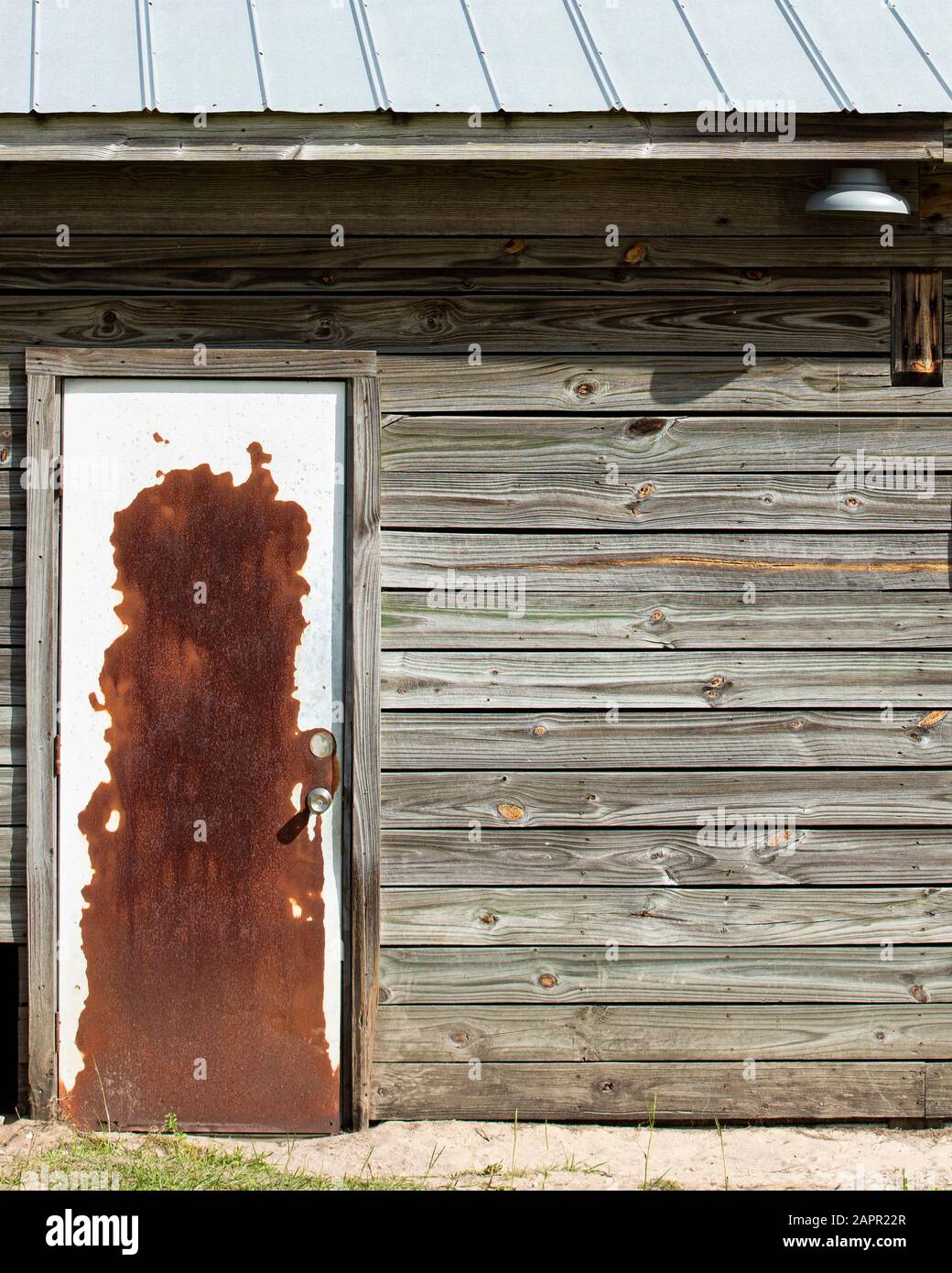 Antiguo granero con puerta oxidada y techo de hojalata. Revestimiento de madera. Luz de granero. Foto de stock