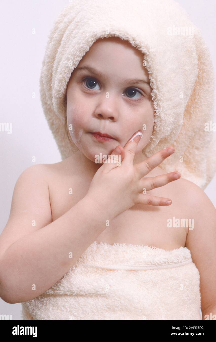 niña pequeña después de baño o ducha con toalla alrededor del cuerpo y la  cabeza poniendo crema en su cara con sus dedos Fotografía de stock - Alamy