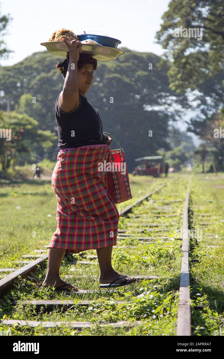 Mujer birmana llevando bandeja de comida sobre su cabeza, cruzando un ferrocarril Foto de stock