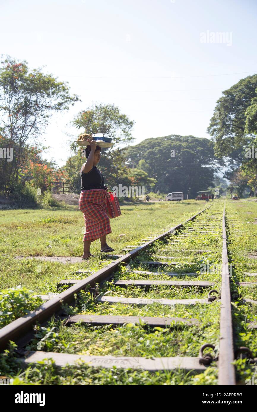 Mujer birmana llevando bandeja de comida sobre su cabeza, cruzando un ferrocarril Foto de stock
