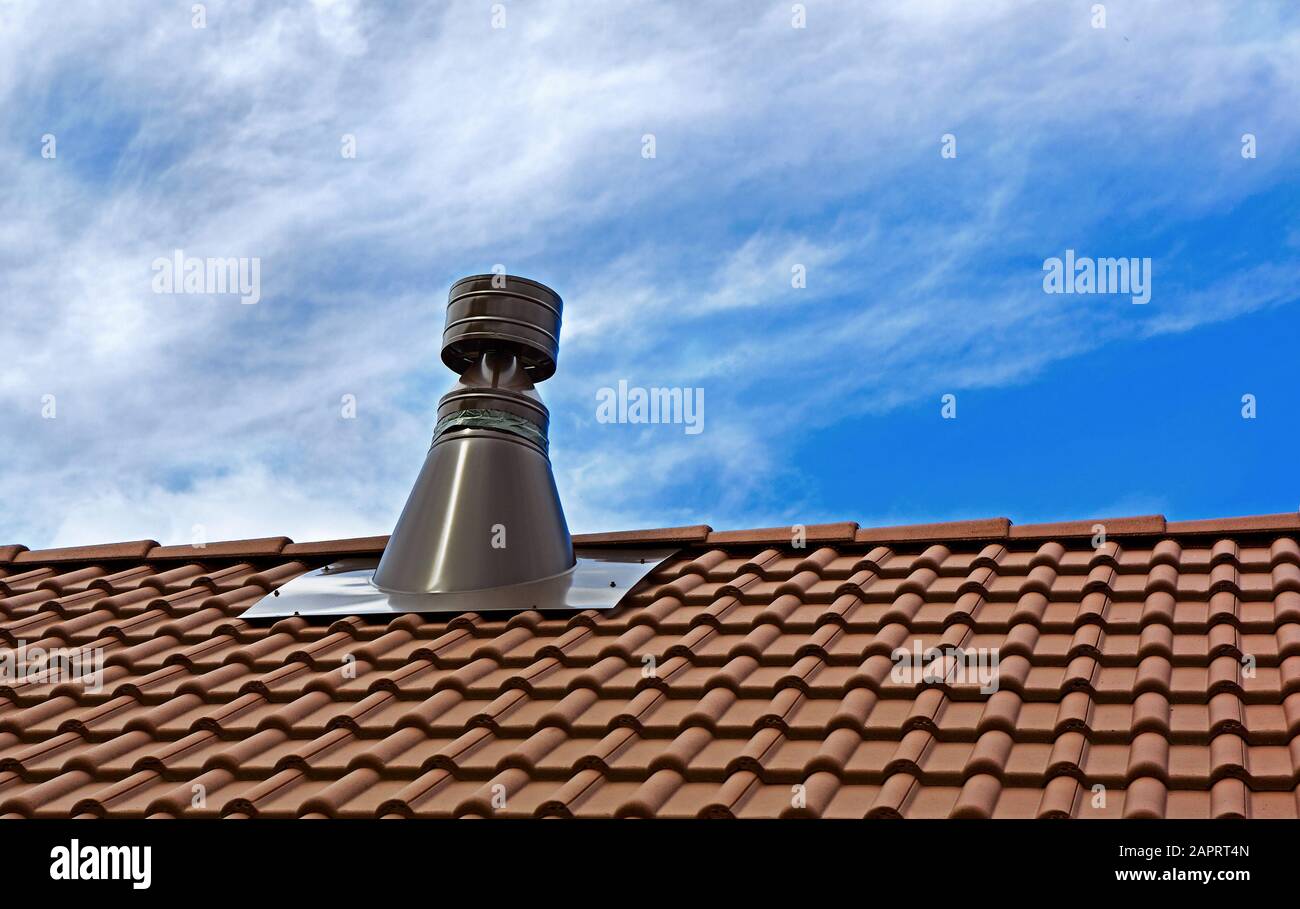 Chimenea de acero inoxidable en el techo de baldosas. Chimenea contra el cielo azul. Foto de stock