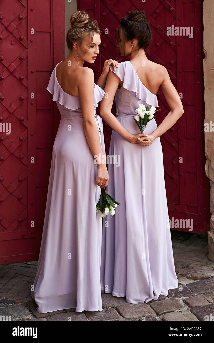 Dos hermosas damas de dama de rubia y morena que visten elegante largo lavanda violeta tulle hombro dama de honor vestido y celebración Fotografía de stock Alamy