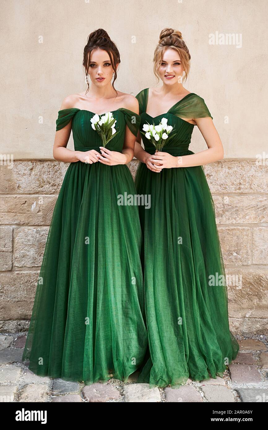 Dos hermosas damas de dama de honor rubia morena mujeres que llevan elegante longitud completa verde chifón dama vestido y celebración Fotografía de - Alamy