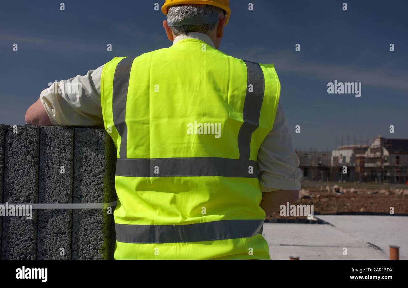 hombre de mediana edad de pelo gris que lleva chaleco de alta visibilidad y dura salud y seguridad en la construcción de obras en el norte de irlanda reino unido Foto de stock