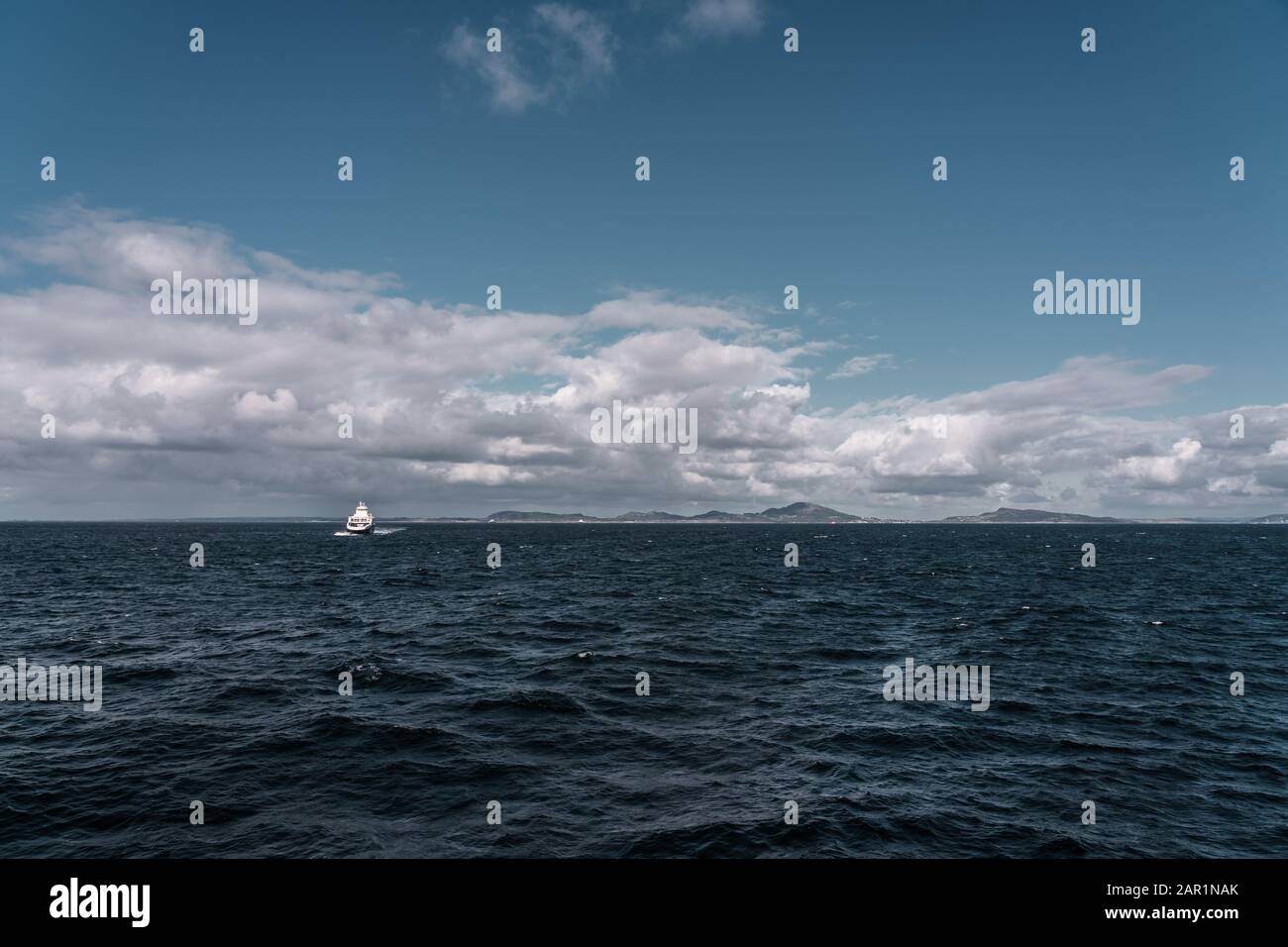 Uno de los ferries entre Mortavika y Arsvågen navegando en mar duro con algunas olas grandes y paisaje de montañas en el fondo, Noruega Foto de stock