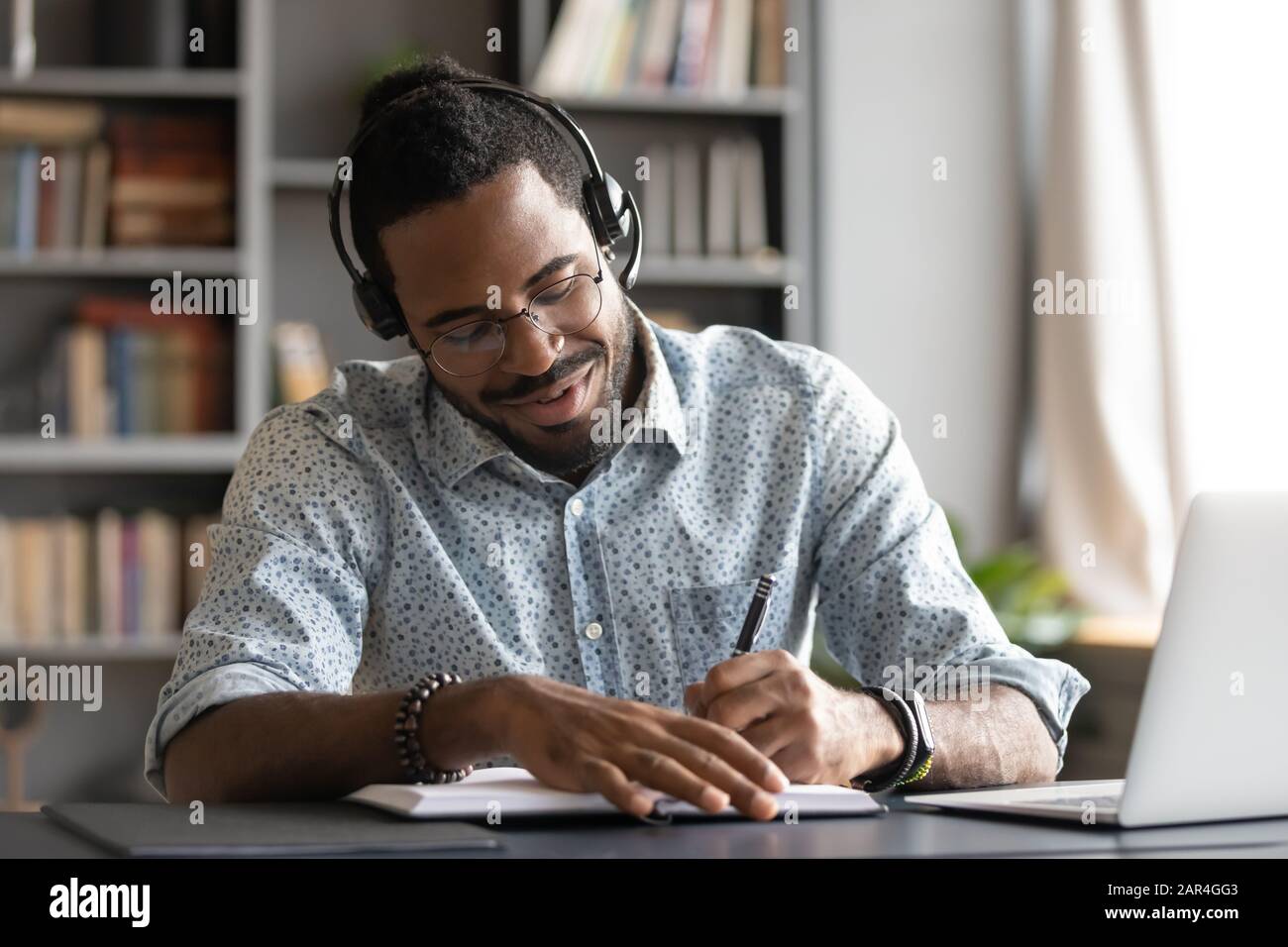Sonriente profesional de estudiantes africanos llevar auriculares eleearing hacer notas Foto de stock