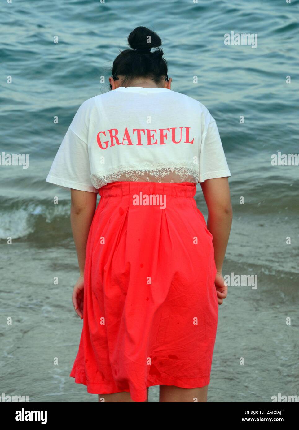 Una chica que lleva una blusa con la palabra "Agradecido" en la parte  trasera mira al mar en el complejo de Nha Trang en Vietnam, Asia, en un día  caluroso y soleado