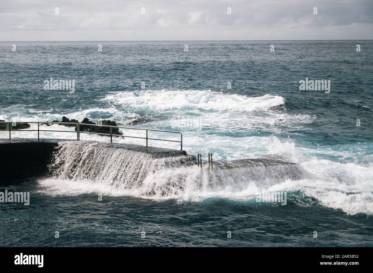 Olas salvajes en la piscina de rocas. Entrada al océano Atlántico con pasamanos en Puerto de la Cruz, Tenerife, Islas Canarias, España Foto de stock