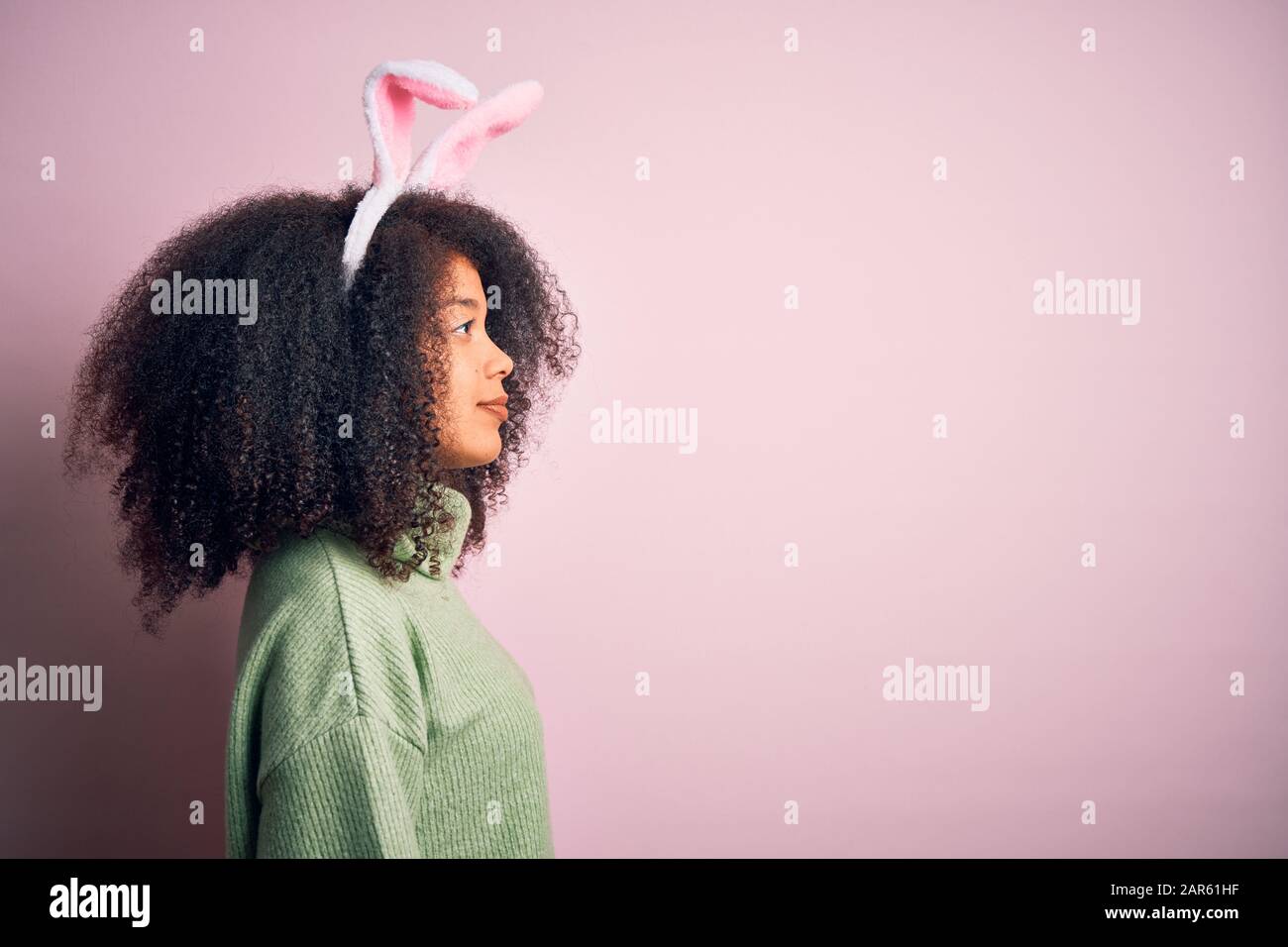 Joven afroamericana con pelo afro usando orejas de conejo de pascua disfraz  sobre fondo rosa mirando al lado, perfil de relax pose con f natural  Fotografía de stock - Alamy