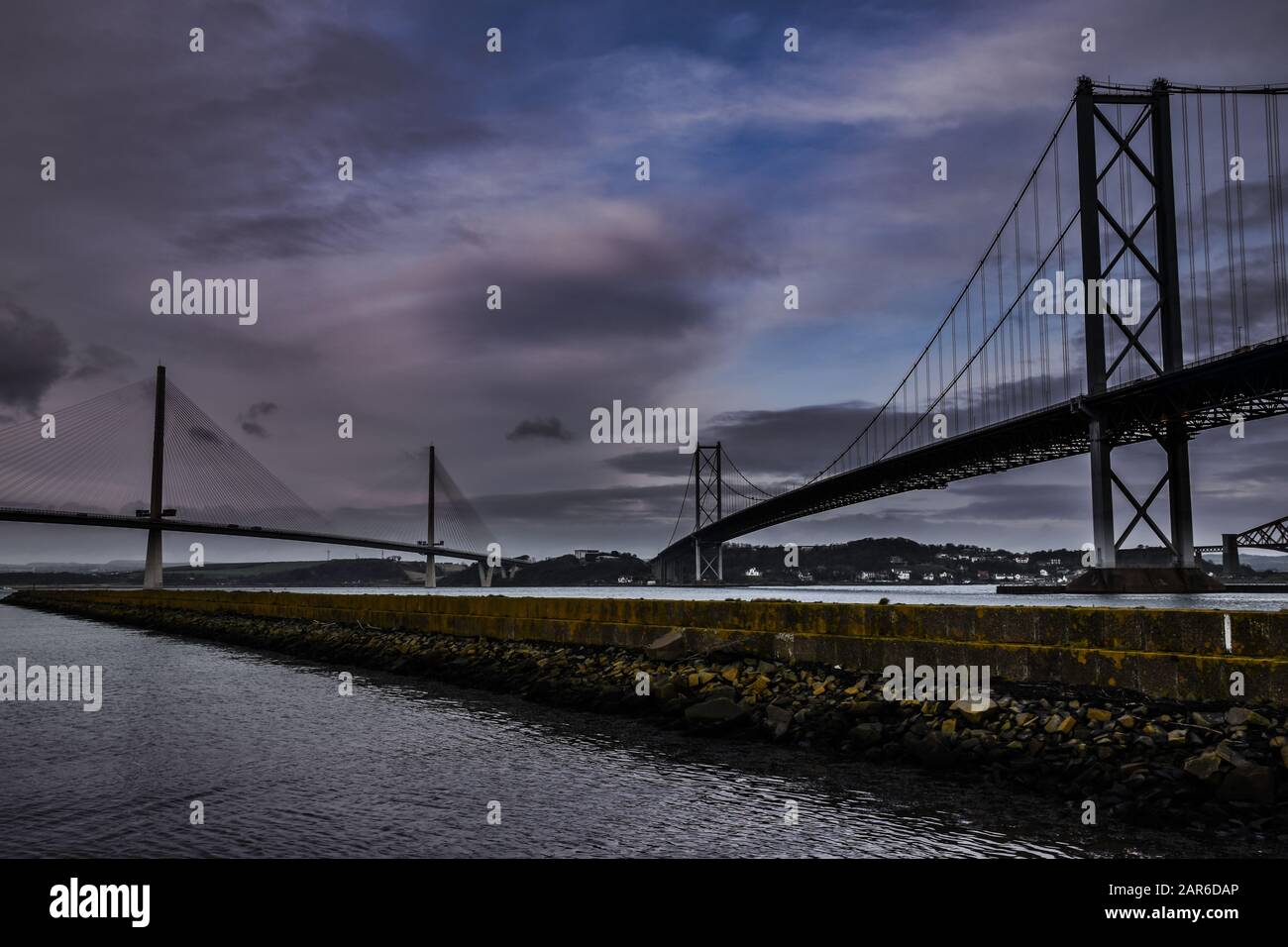 Forth Road Bridge y Queensferry cruce puentes sobre El estuario Forth en Escocia con cielos dramáticos, muelle en primer plano Foto de stock