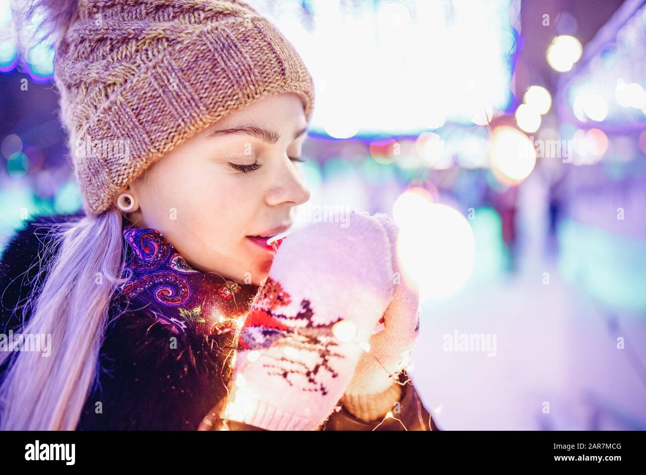 La chica sostiene un vaso de cartón con café o té caliente en invierno en manoplas calientes Foto de stock