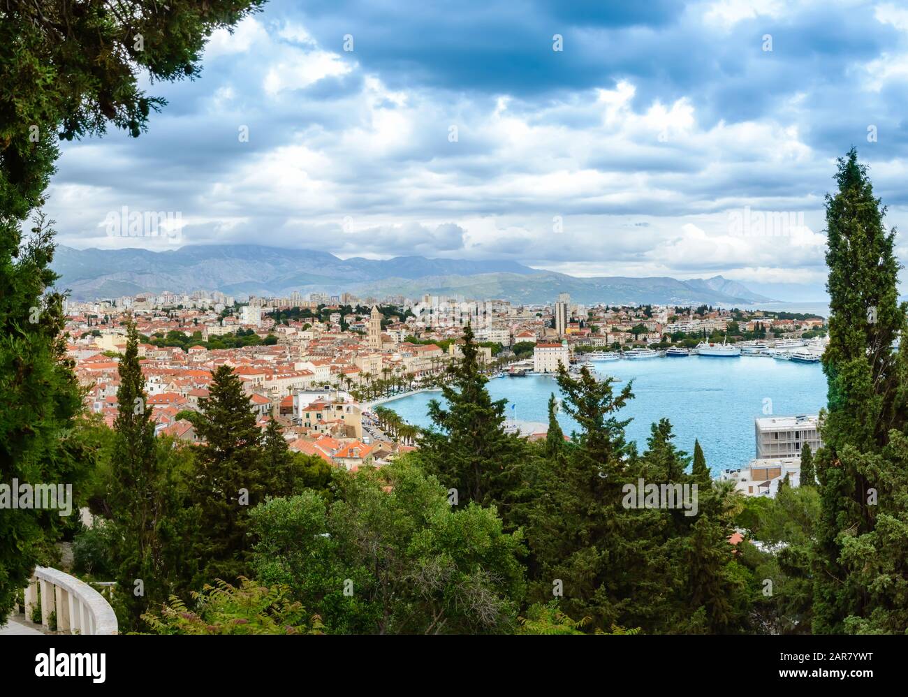 Split, Croacia: Vista sobre el casco antiguo con coloridos edificios, Riva Promenade, palmeras y la bahía desde la colina de Marjan. Montañas en el fondo, los árboles en Foto de stock