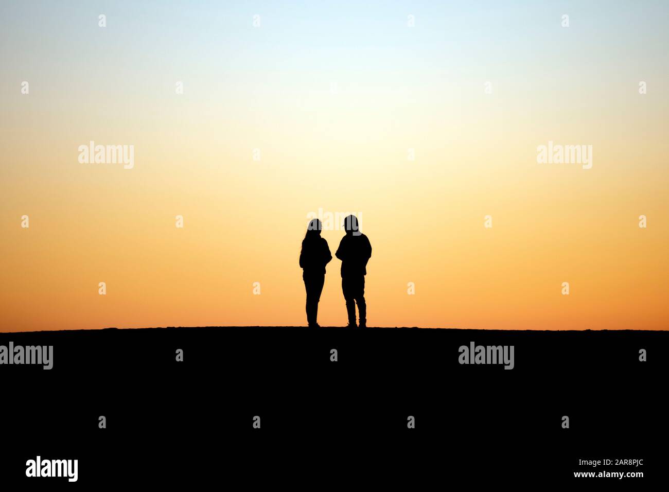 Dos personas siluetas contra el cielo crepuscular se encuentran juntas lado a lado Foto de stock