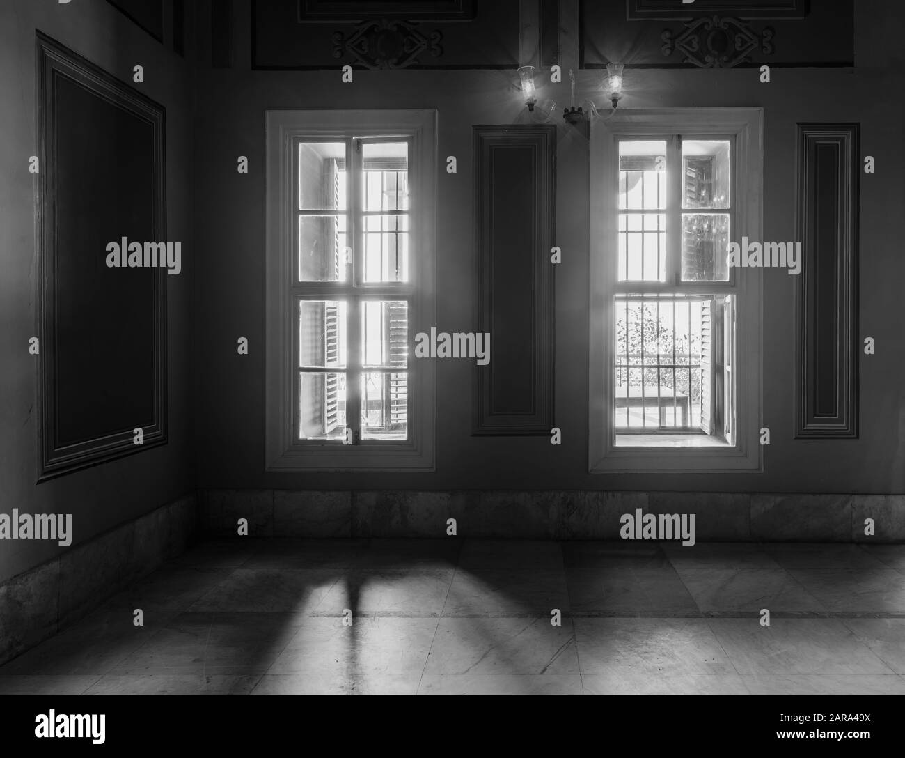 Blanco y negro captura de alto contraste de dos ventanas estrechas, revelando una fuerte luz en la habitación oscura con suelo de mármol blanco azulejado Foto de stock