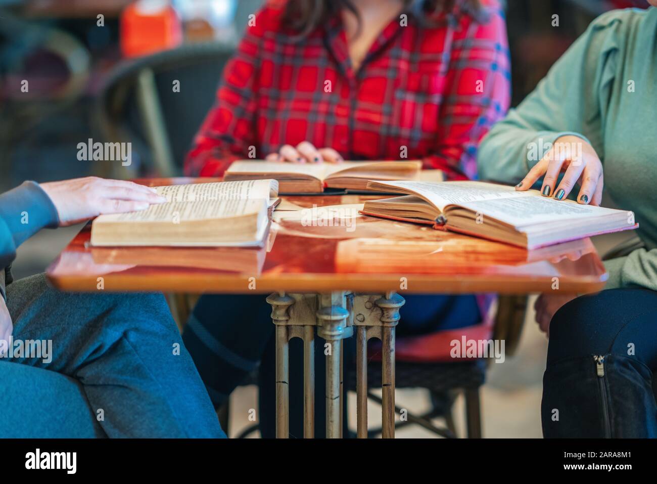 Tres mujeres intelectuales sentadas y leyendo libros en la biblioteca o cafetería Foto de stock