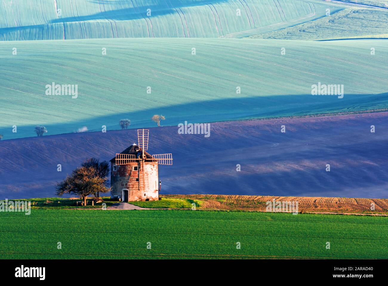Precioso paisaje rural con antiguo molino de viento y verdes colinas soleadas de primavera. Región De Moravia Del Sur, República Checa Foto de stock
