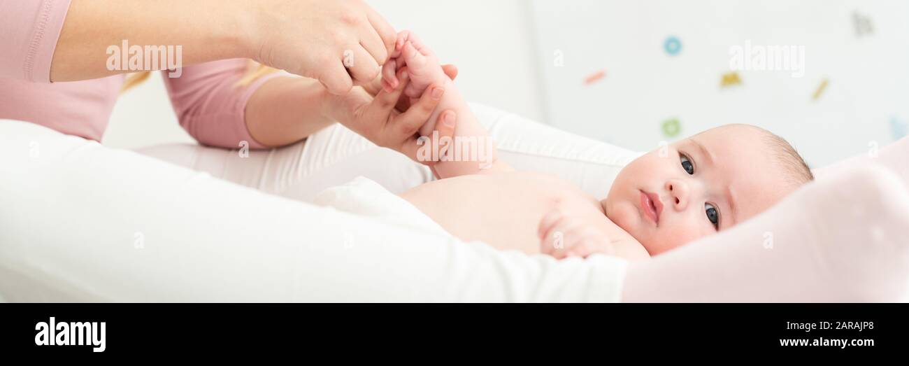 Banner de masaje para bebés. Madre masajear suavemente su Baby Boy mientras aplica loción para el cuerpo para su piel. Bebé acostado sobre la espalda y mirando a la cámara. Foto de stock