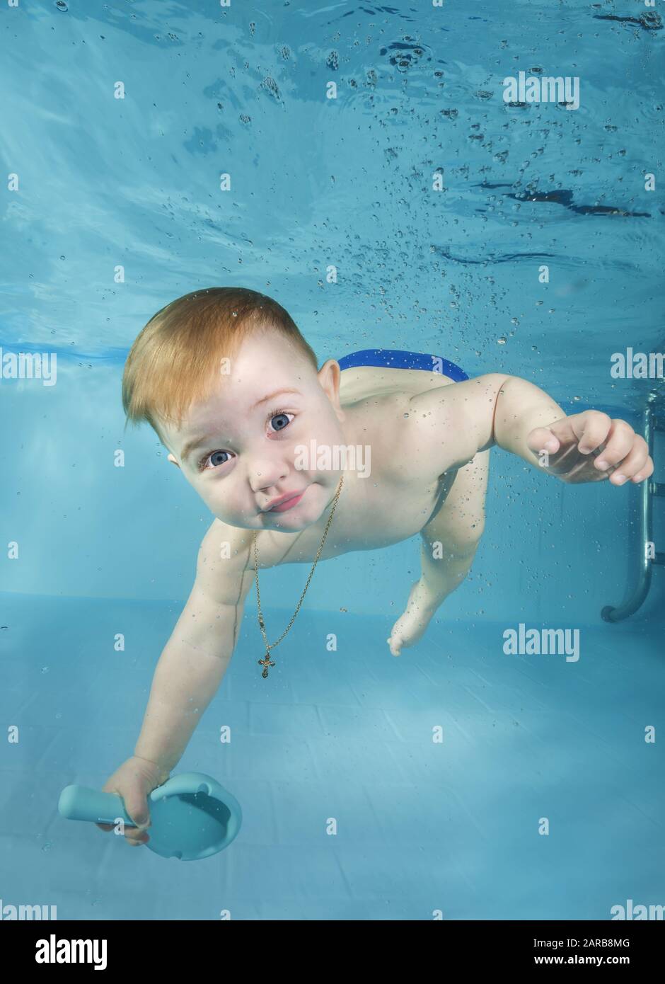 Divertido niño con juguete juega bajo el agua con diversión en la piscina. Estilo de vida familiar saludable y actividades deportivas acuáticas para niños. Desarrollo infantil, enfermedad Foto de stock