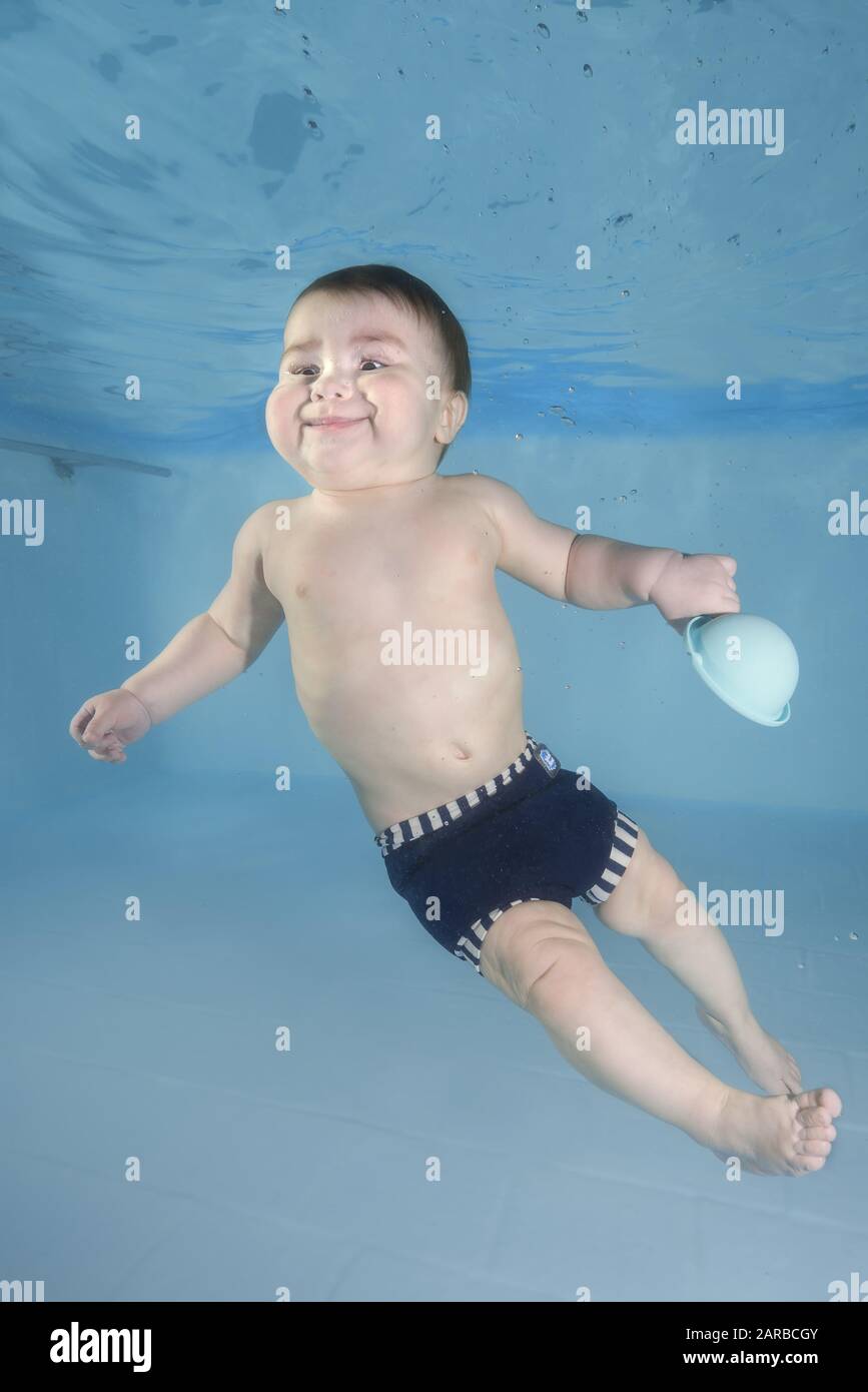 El niño pequeño aprende a nadar bajo el agua. Bebé con juguete nadando bajo el agua en la piscina. Estilo de vida familiar saludable y actividades deportivas acuáticas para niños Foto de stock